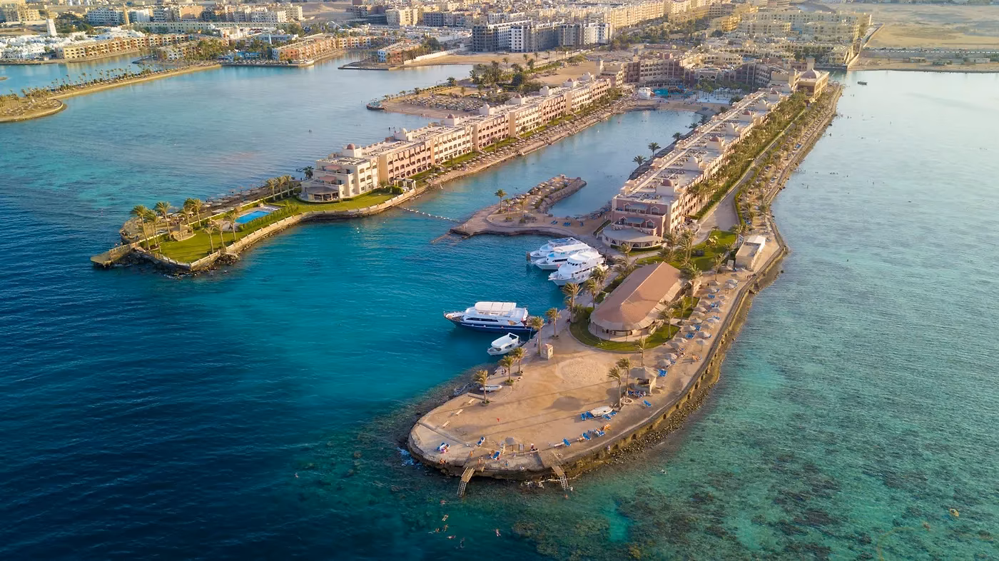 Luchtfoto van een schiereiland met hotelgebouwen en een kade met boten aan helder turkoois water