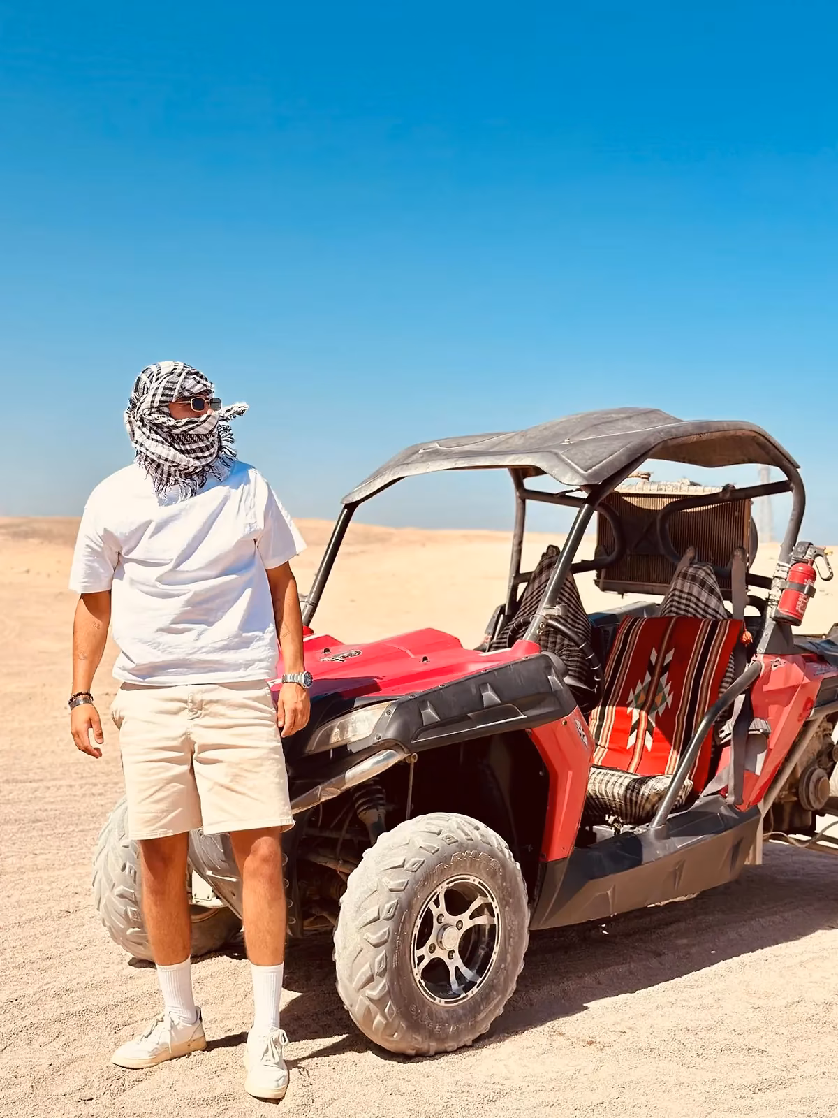 Een man met een hoofddoek bij een rode buggy in de woestijn