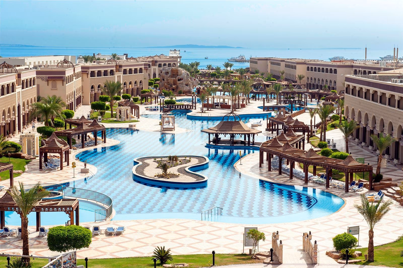 Zwembad met een plantenrijk eiland en pergola's op het terrein van Sentido Mamlouk Palace Resort in Hurghada, met zicht op zee