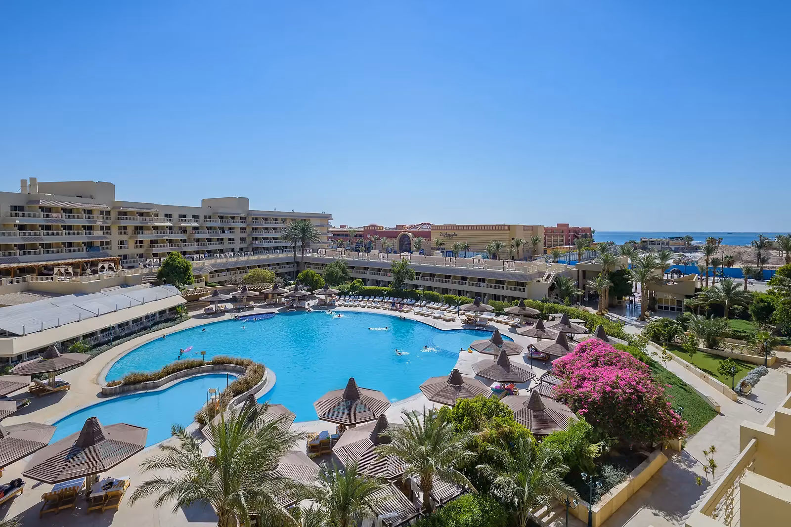 Het hoofdzwembad van Sindbad Club in Hurghada met bloeiende bougainville, de hotelvleugels en de Rode Zee op de achtergrond