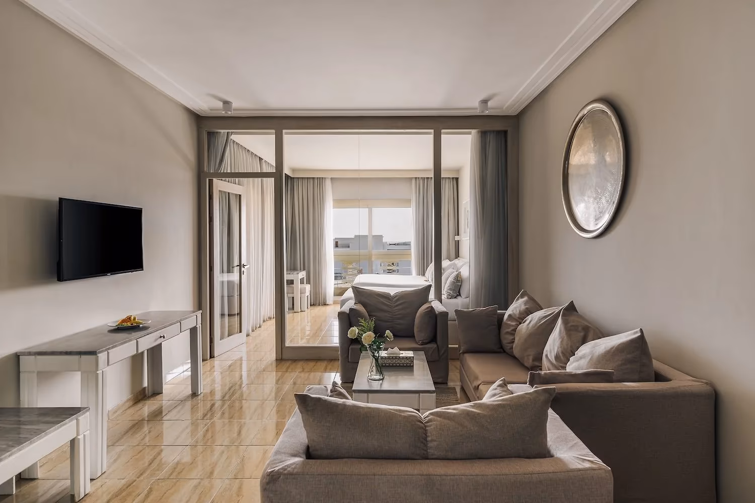 Woonkamer van de Deluxe familiesuite met grijze hoekbank en glazen wand naar de slaapkamer in Hotel Sindbad Club in Hurghada