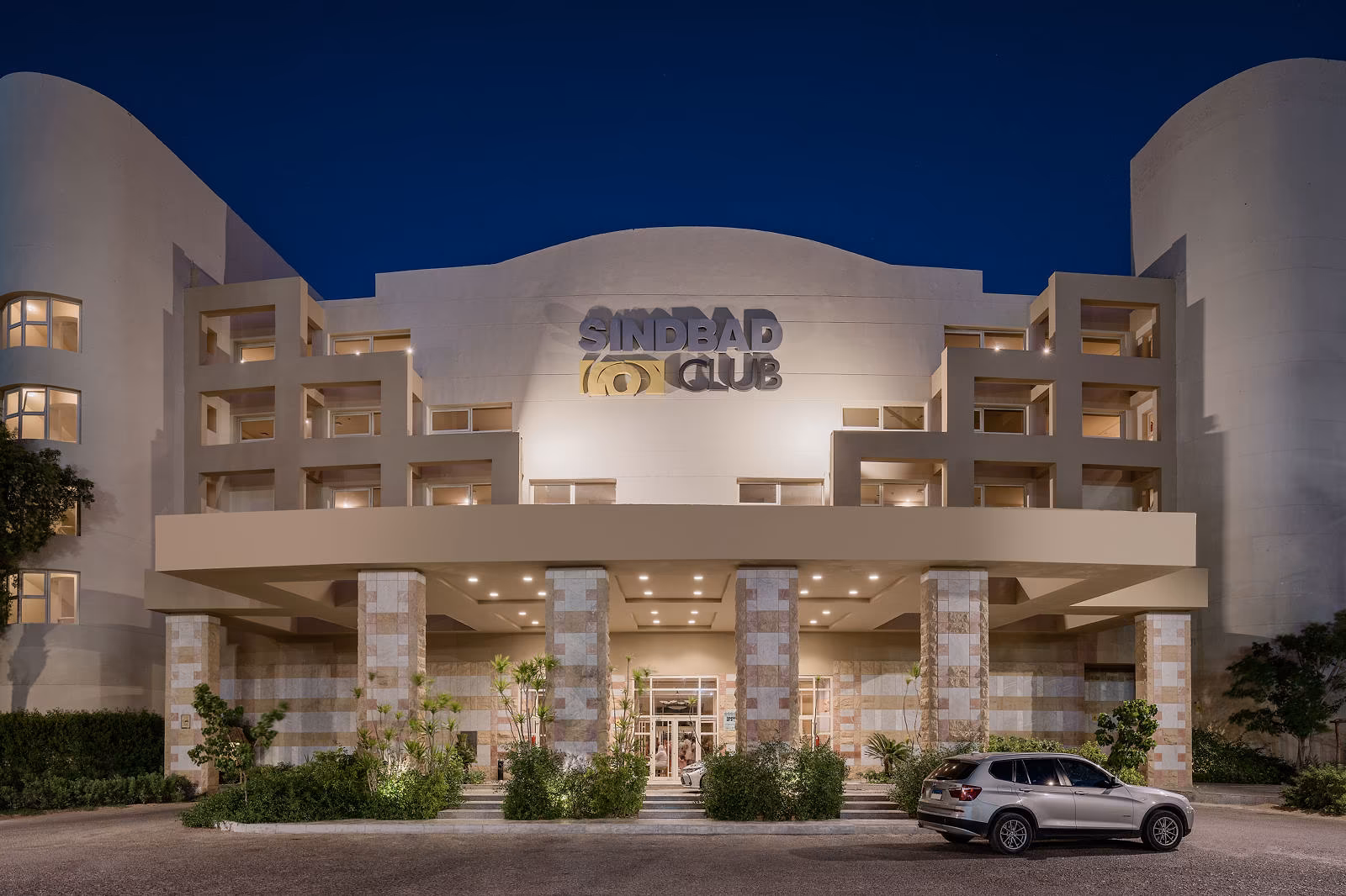 De verlichte hoofdingang van Hotel Sindbad Club in Hurghada met het Sindbad Club-logo op de gevel