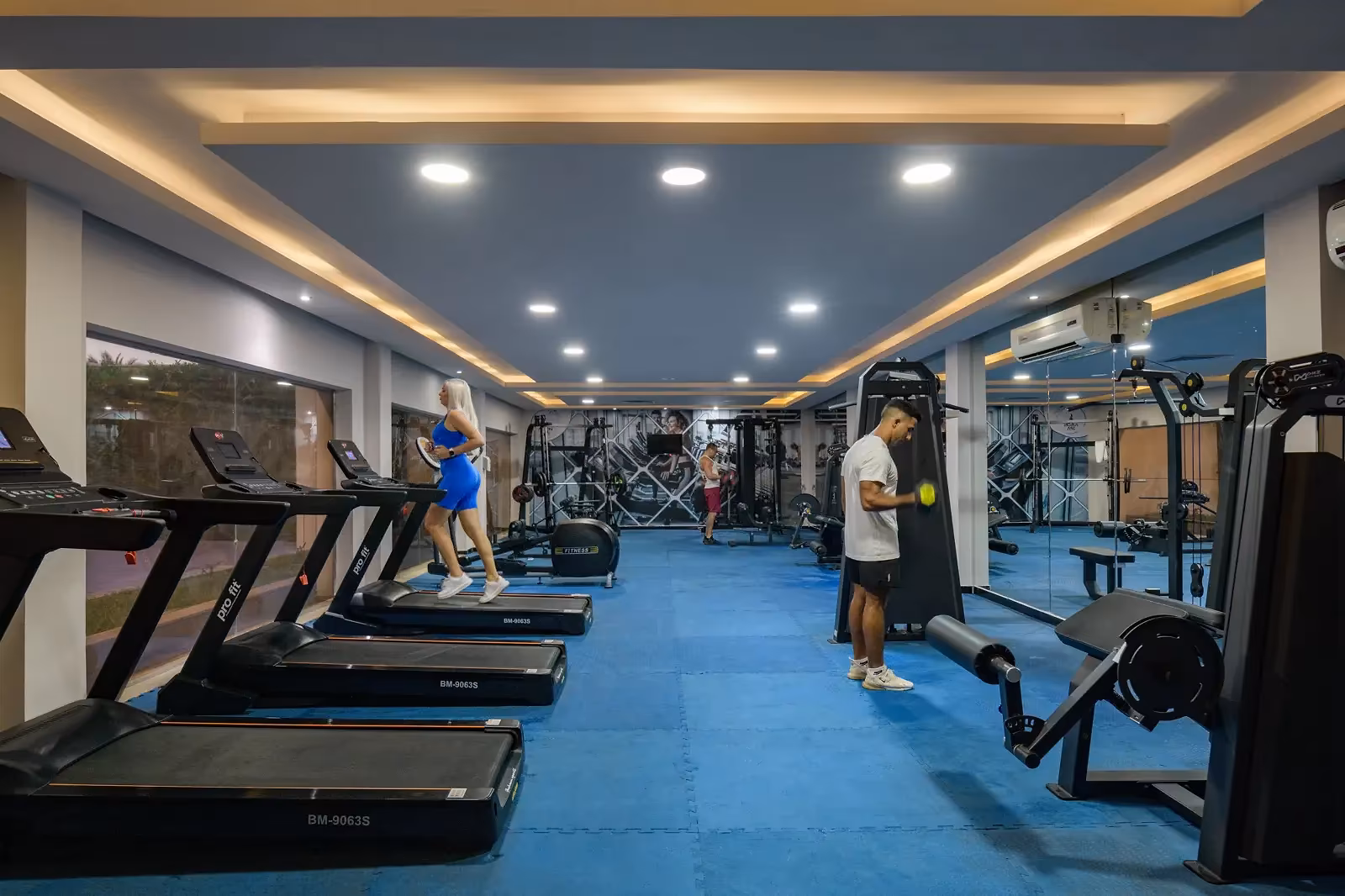 Fitnessruimte met een blauwe sportvloer, een rij loopbanden langs de ramen en krachtapparaten aan de overkant in Sindbad Club in Hurghada