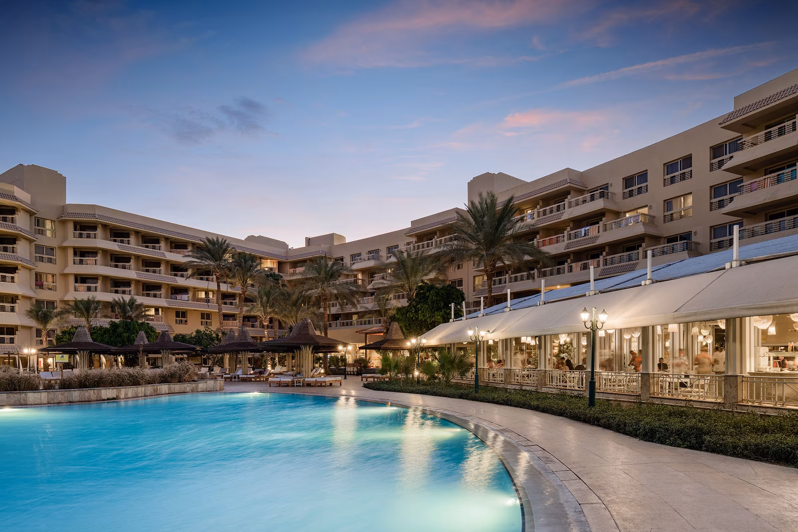 Het hoofdzwembad bij schemering met de hotelvleugels en het verlichte terrasrestaurant van Hotel Sindbad Club in Hurghada