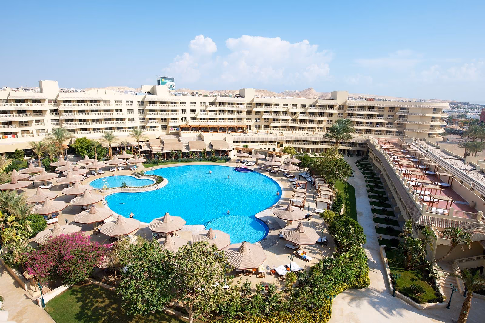 Het ronde hoofdzwembad van Sindbad Club in Hurghada met rieten parasols, het hoofdgebouw en de bergen op de achtergrond