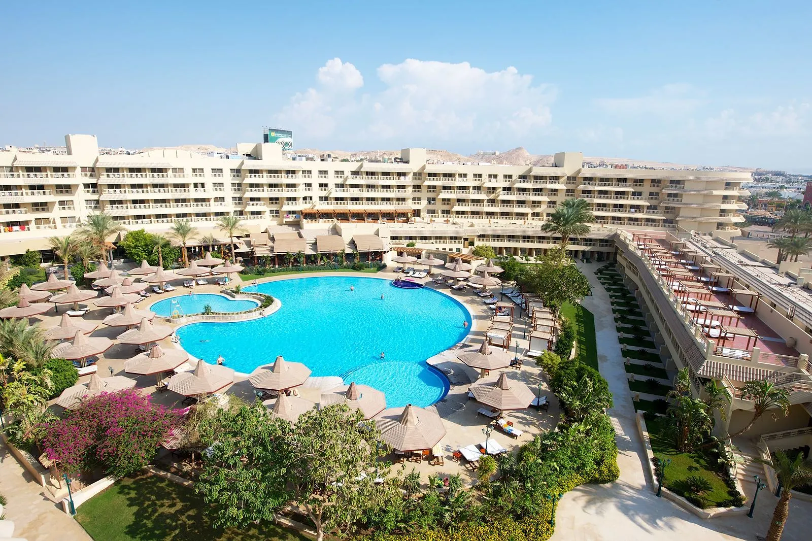 Luchtfoto van het grote ronde hoofdzwembad met parasols en het hoofdgebouw van Sindbad Club in Hurghada, met kale bergen op de achtergrond