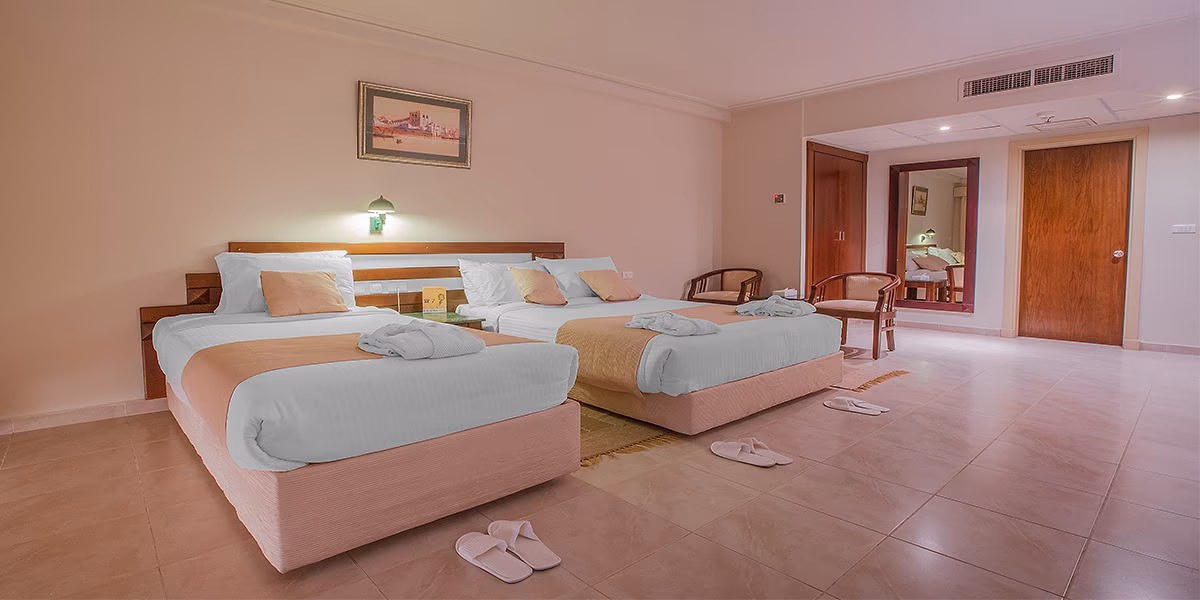 Kamer in oudere inrichting met twee losse bedden met perzikkleurige lopers, een tegelvloer, houten deuren en een spiegel bij Sindbad Club in Hurghada