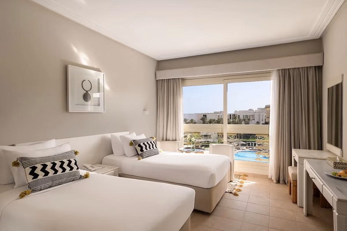 Kamer met twee eenpersoonsbedden en een groot raam met zicht op het zwembad in Hotel Sindbad Club in Hurghada