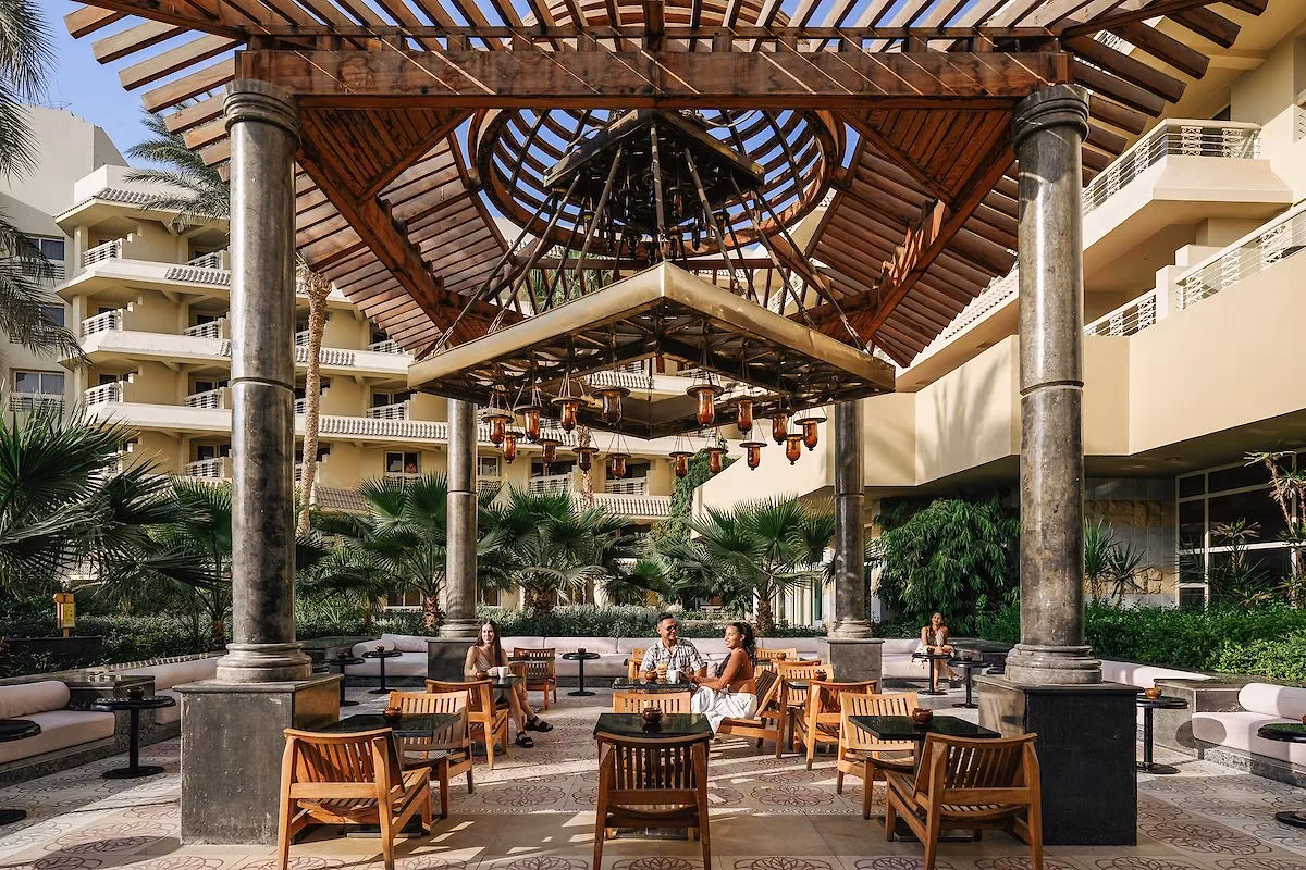 Gasten aan tafels onder de houten pergola van de Mastaba-lounge overdag bij Hotel Sindbad Club in Hurghada