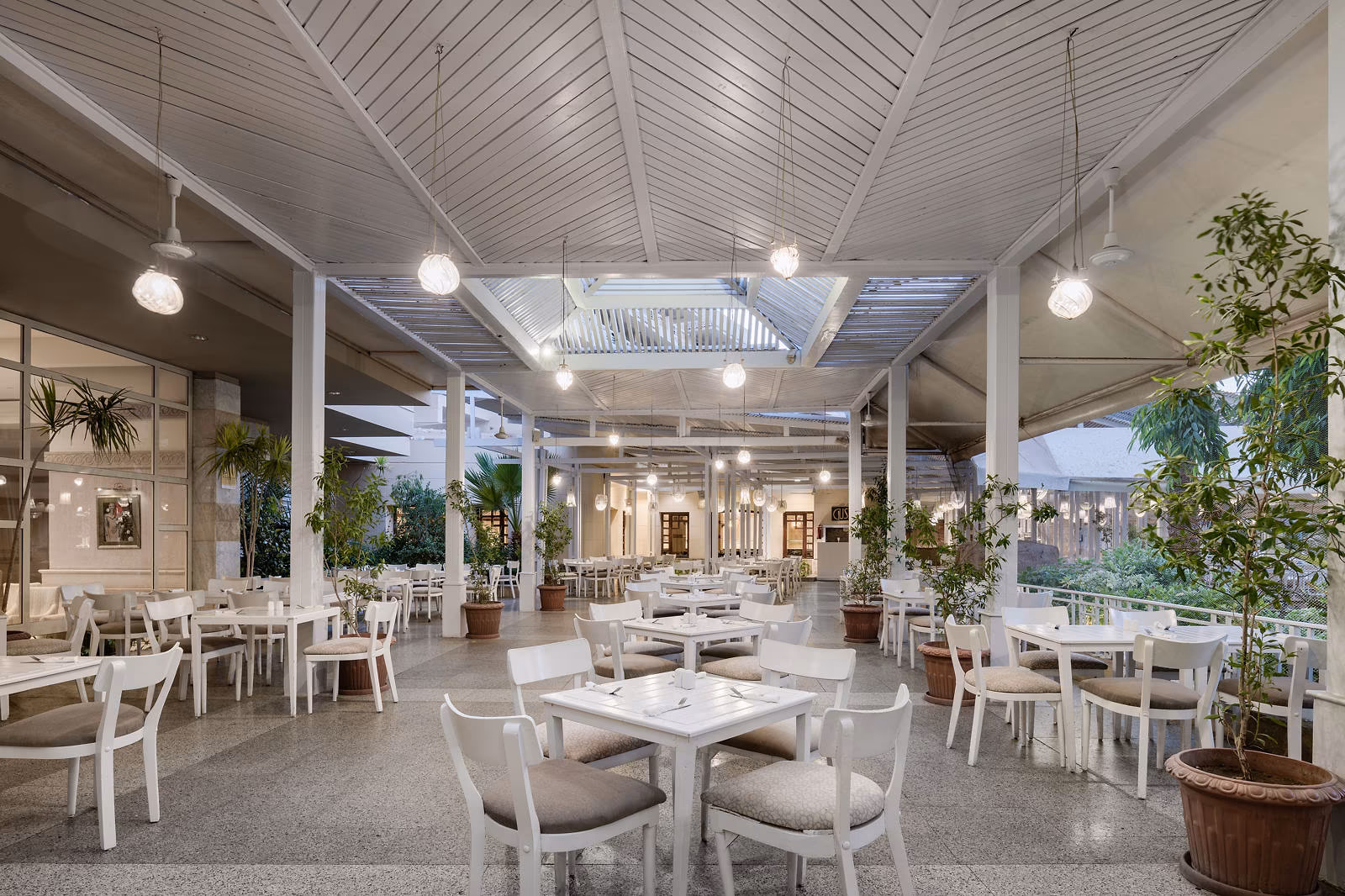 Overdekt terrasrestaurant met witte stoelen, hanglampen en planten bij Hotel Sindbad Club in Hurghada