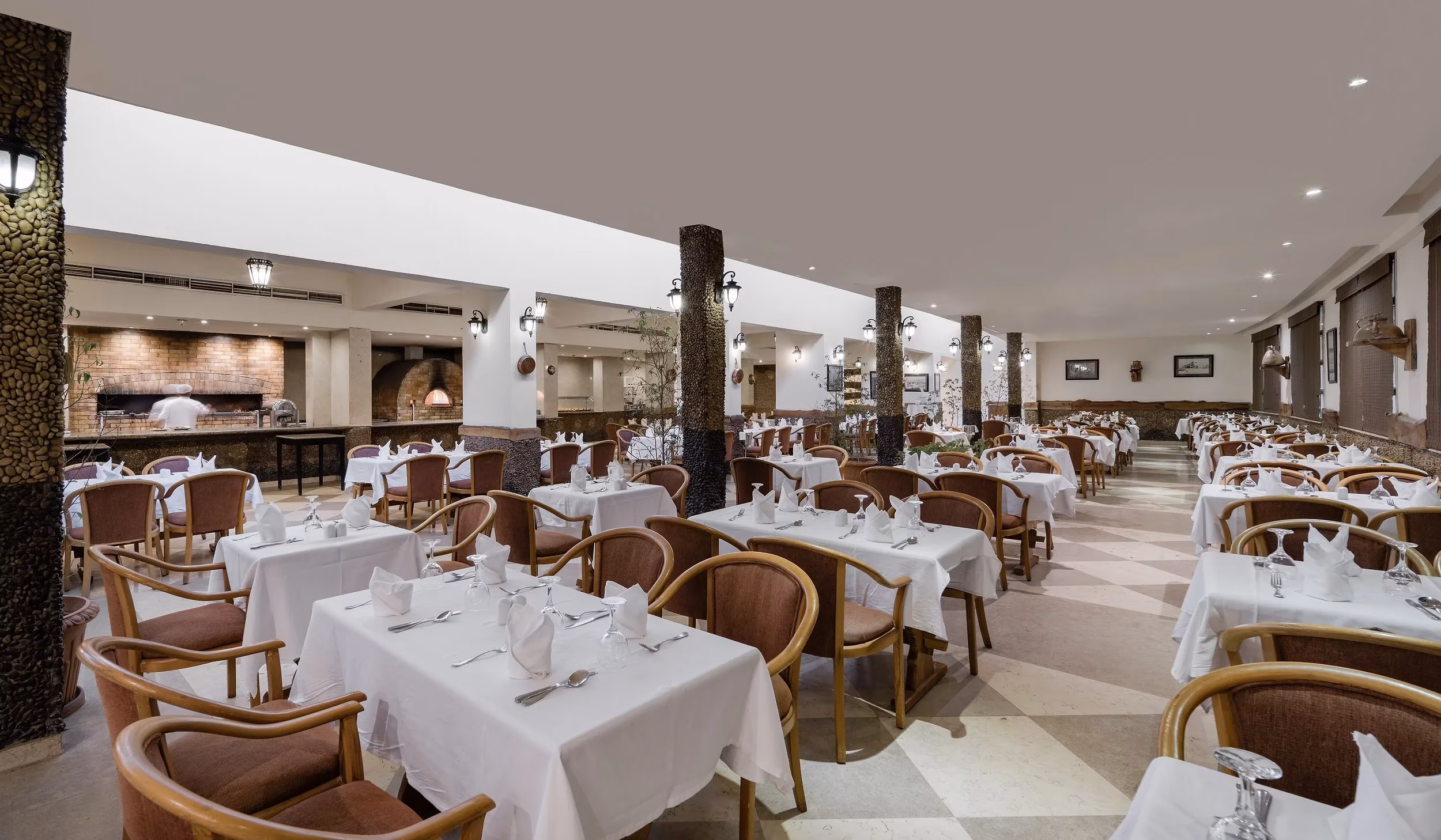 Restaurantzaal met witte tafelkleden, geblokte vloer en een steenoven in Hotel Sindbad Club in Hurghada