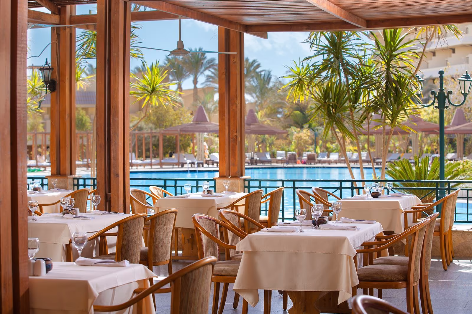 Overdekt terrasrestaurant met gedekte tafels en houten stoelen, met uitzicht op het zwembad en palmen bij Sindbad Club in Hurghada