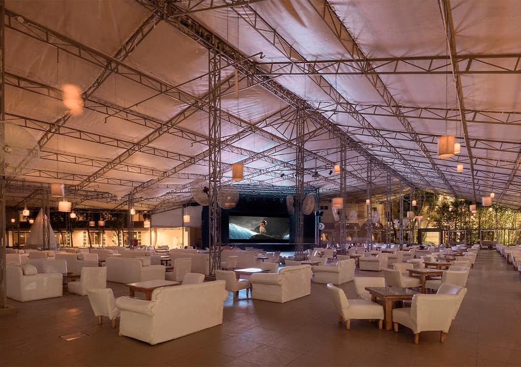 Overdekte showzaal onder een tentdak met witte loungebanken, lampions en een groot podiumscherm in Sindbad Club in Hurghada
