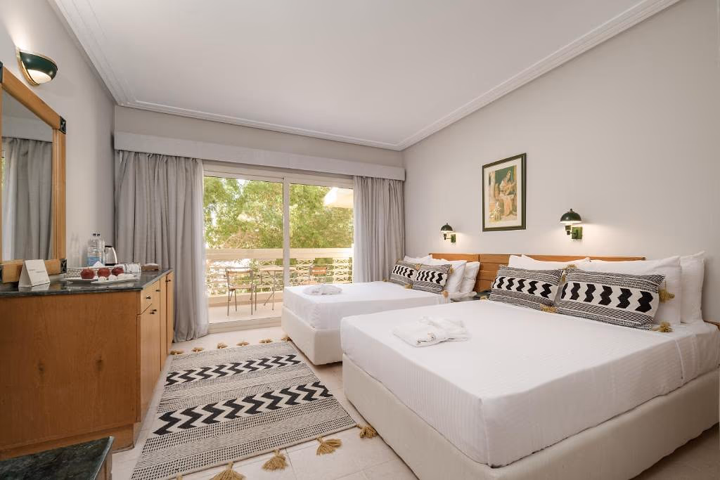Kamer met twee grote bedden met zwart-wit kussens, een houten kast en een balkon tussen groene bomen in Sindbad Club in Hurghada