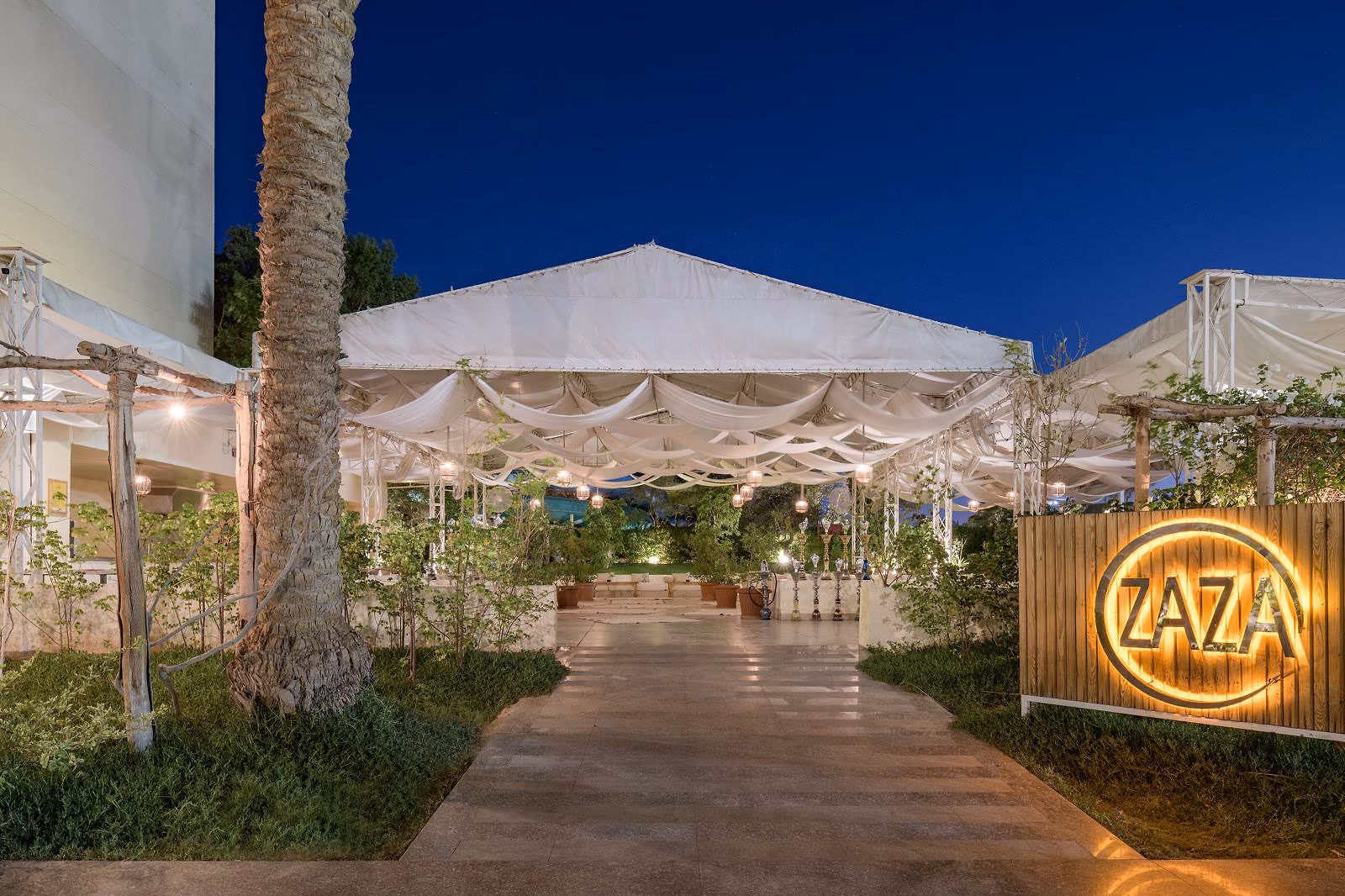Ingang van de Zaza-lounge met verlicht naambord en tentdaken in de avond bij Hotel Sindbad Club in Hurghada