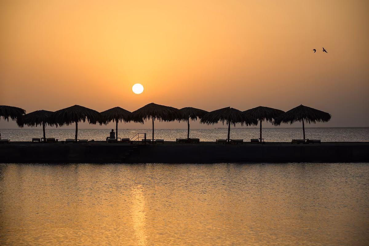 Zonsopkomst boven de Rode Zee met rieten parasols op de pier van Hotel Sindbad Club in Hurghada