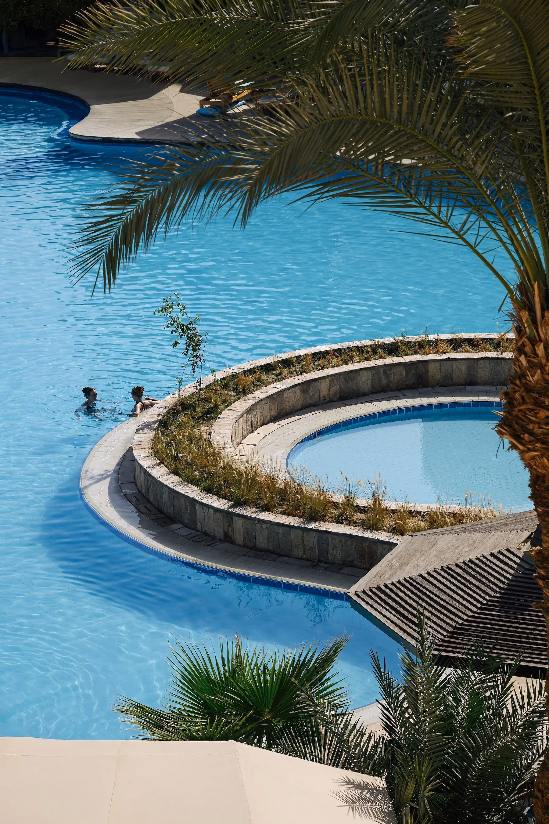 Zwembad met een rond eilandje met planten en palmbladeren op de voorgrond bij Hotel Sindbad Club in Hurghada